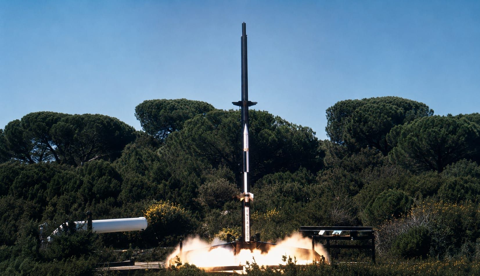 Lanzamiento de un cohete sonda desde su rampa entre pinos, con la ignición del motor en la base.